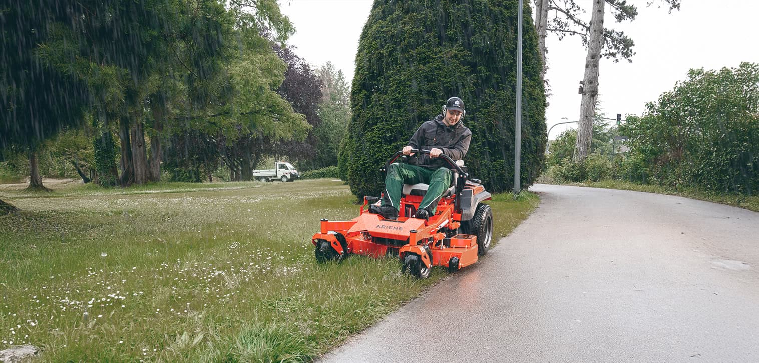 Professional mowing with an Ariens zero-turn mower on a wet lawn in rainy conditions