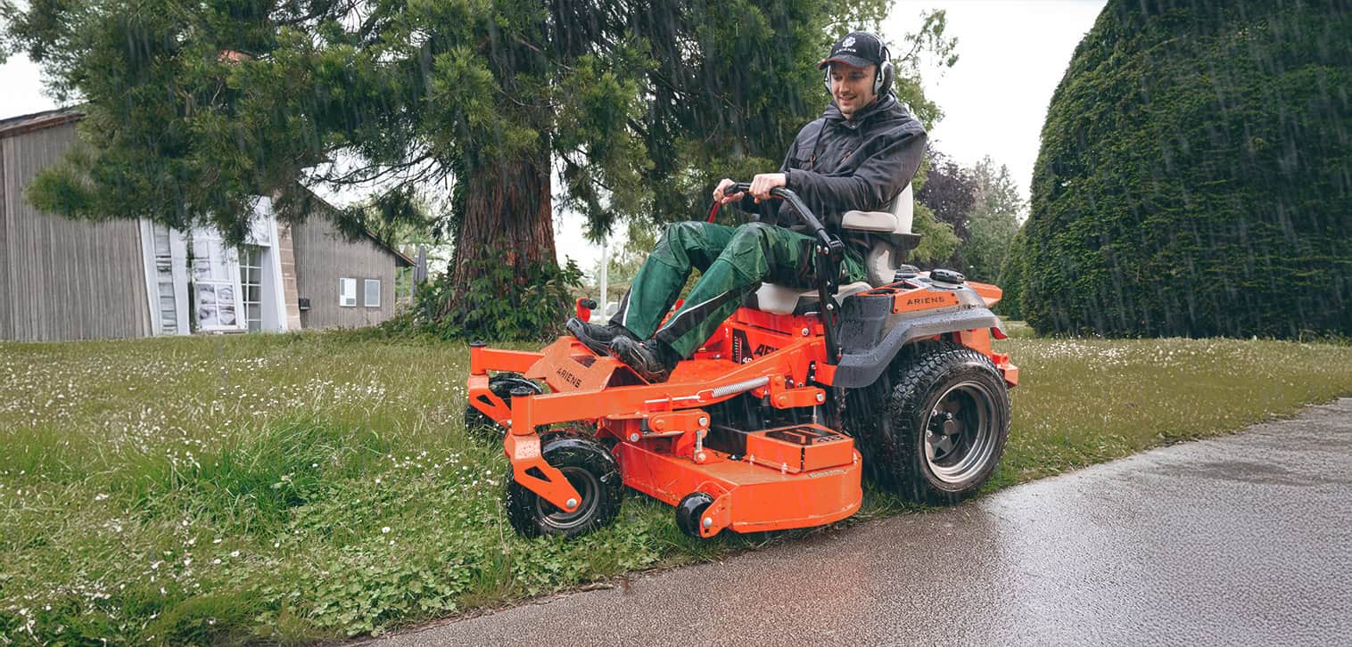 Professional mowing with an Ariens zero-turn mower on a wet lawn in rainy conditions