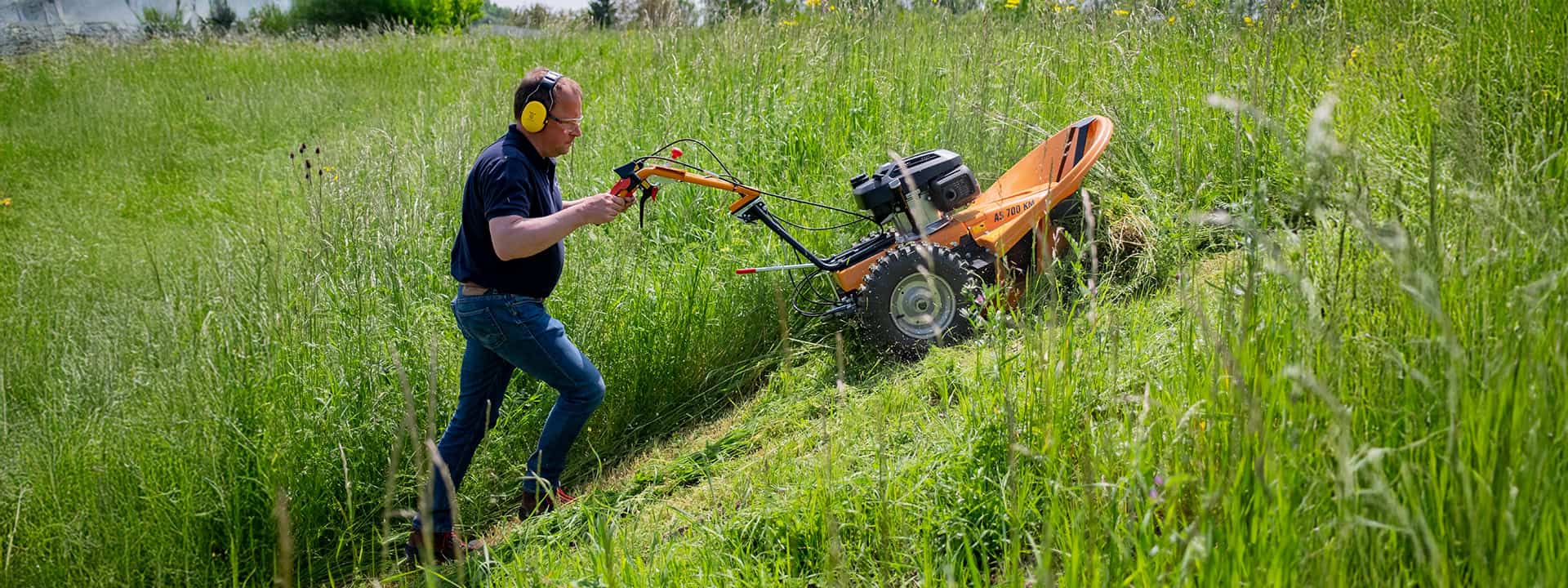 Man using an AS-Motor disk mower on a steep slope, cutting highgrass