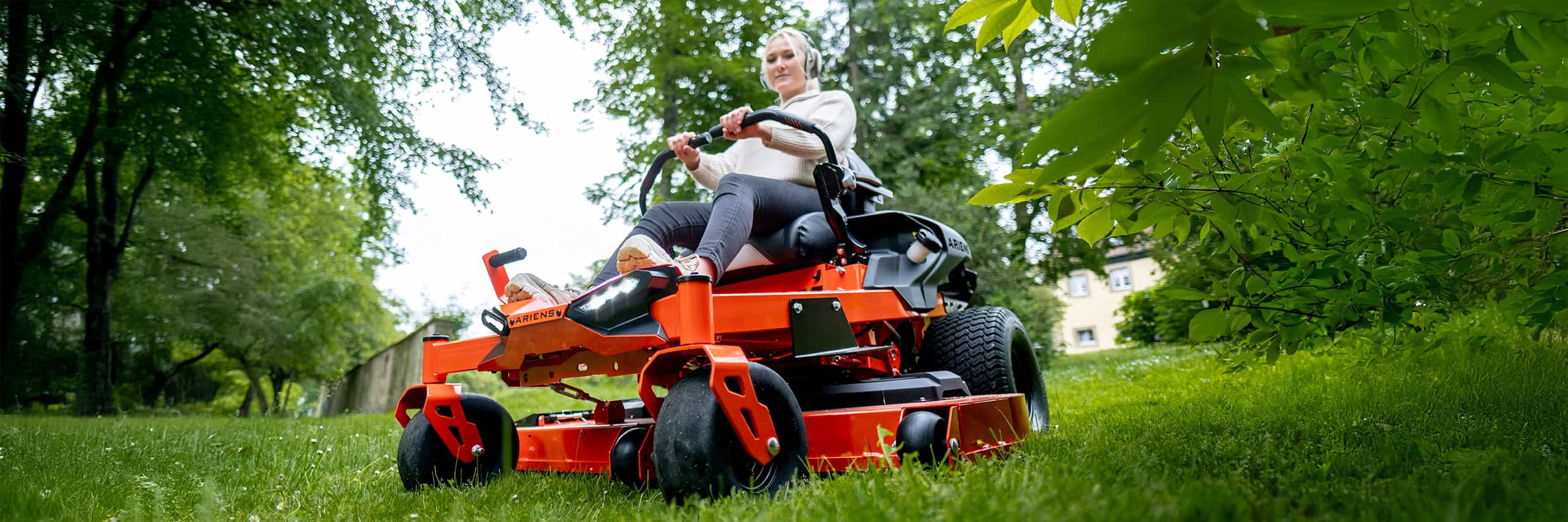 Wide close-up shot of a Ariens Zero-Turn mower IKON, a woman mowing lawn