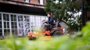 Smiling man driving a Ariens Zero-Turn mower across the lawn, having fun mowing grass