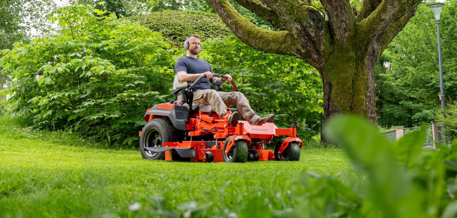 Ariens Zero-Turn Mower model APEX, showcasing efficient mowing with zero-turn features. Happy young man is mowing the lawn with an Ariens Zero-Turn mower