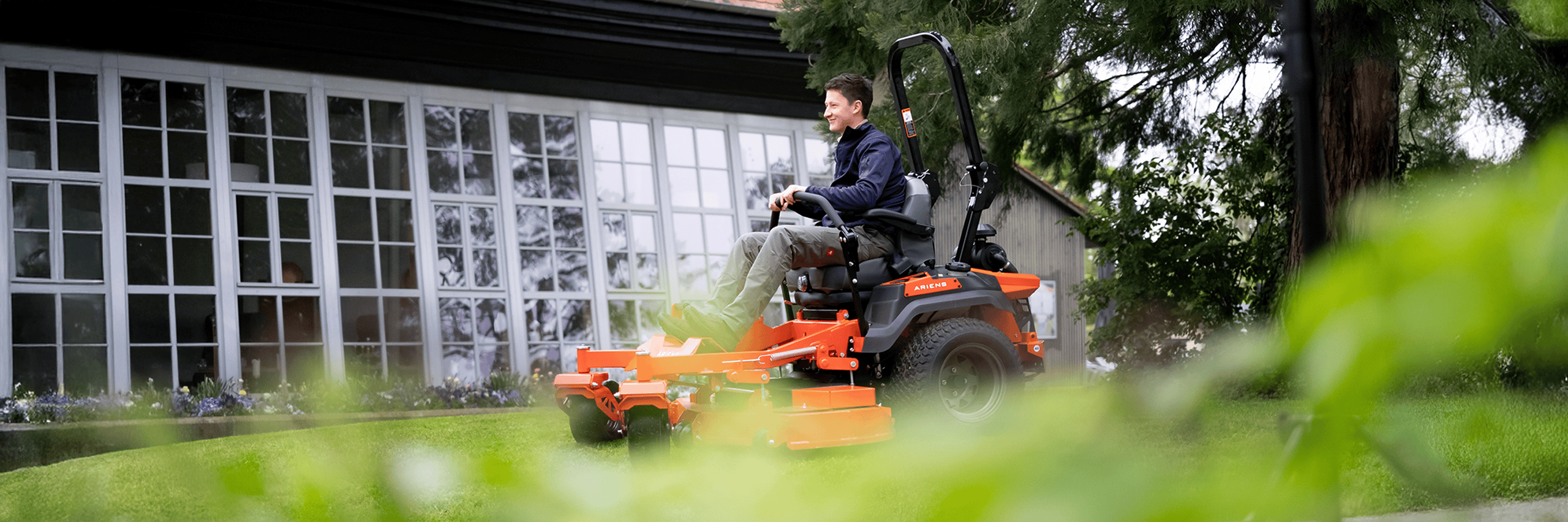 Smiling man driving a Ariens Zero-Turn mower across the lawn, having fun mowing grass
